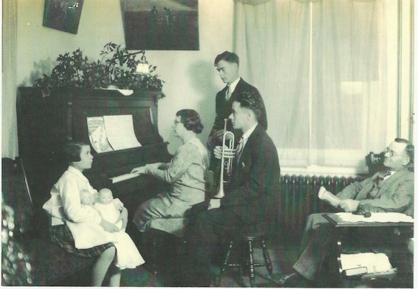 A young Geraldine sits with her dolls while her mother and brothers entertain as her father looks on in approval.